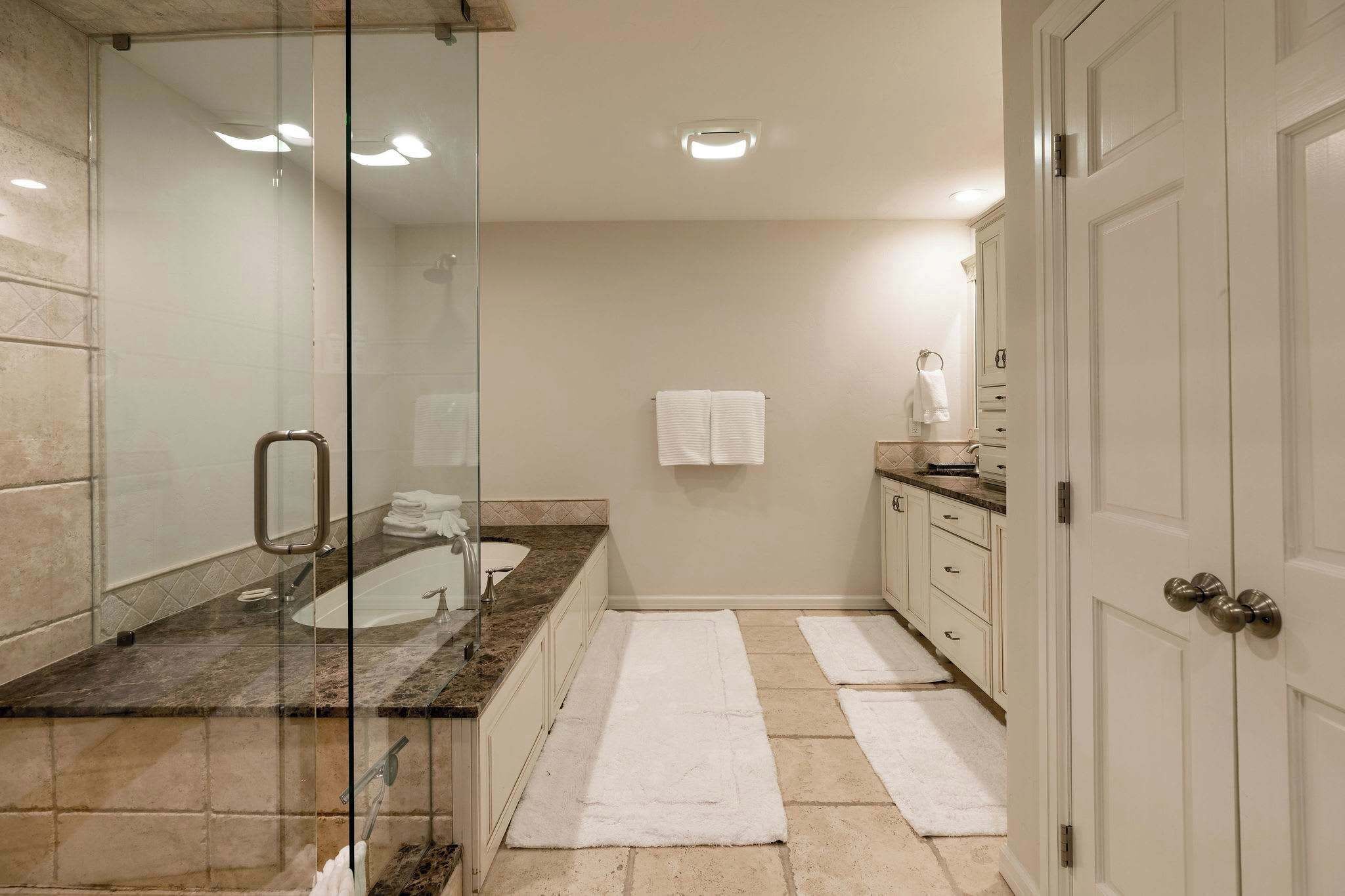 A bathroom with a glass-enclosed shower, a sink with a marble countertop, and a white towel hanging on the wall.