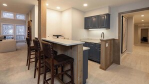 A modern kitchen with a bar area, wooden chairs, and dark cabinets. - NEWLY RENOVATED! Expansive 8,800 SF Luxury Home + Walkable to Beaver Creek Village + Hot Tub + Game Rooms (Beaver Creek)