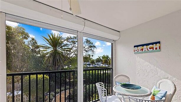A balcony with a view of palm trees and a beach sign. - Sandpebble 2B (Sanibel)