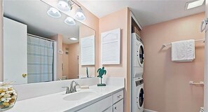 A modern bathroom with a large mirror, a sink, a washing machine, and a towel rack. - Sandpebble 2B (Sanibel)