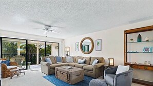 A spacious living room with a large sectional sofa, a coffee table, and a round mirror on the wall. - Sandpebble 2B (Sanibel)
