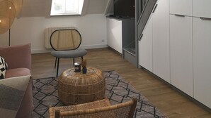A modern loft with high ceilings, exposed beams, and a skylight. There is a cozy seating area with a rattan chair and ottoman, a television, and a staircase with a view to the upper level. - Villa Mathë" apartment, view of Roscoff harbour (Roscoff)