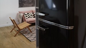 A modern living room with a black Amica refrigerator, a wooden rocking chair, a pink sofa with patterned cushions, and a staircase with a white railing. - Villa Mathë" apartment, view of Roscoff harbour (Roscoff)