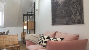 A spacious living room with a high ceiling, a large wall mural, and a cozy seating area with a pink sofa and wicker chairs. - Villa Mathë" apartment, view of Roscoff harbour (Roscoff)