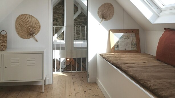 A bedroom with a sloped ceiling, skylights, a bed, a dresser, and a wall-mounted fan. - Villa Mathë" apartment, view of Roscoff harbour (Roscoff)