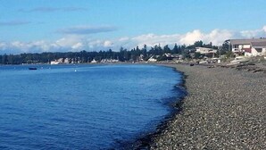 Una playa de guijarros con un mar tranquilo y casas al fondo.