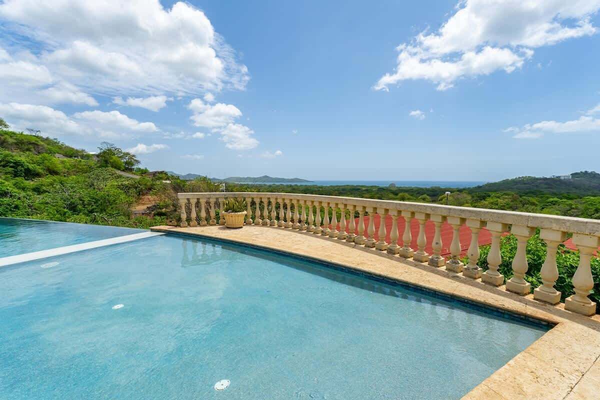 A swimming pool with a balustrade, surrounded by greenery and a clear sky.