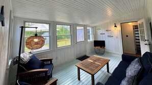A cozy room with a wooden floor, a sofa, a coffee table, and a TV. There are windows with a view of the outside.