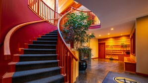 A spiral staircase with wooden railings and carpeted steps, leading to a landing area with a potted plant and a fire feature.