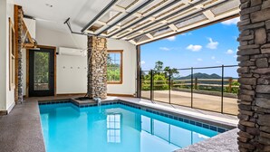 A swimming pool with stone accents, a stone pillar, and a view of mountains through large windows. - Massive Views+Indoor Pool+Movie Theater+Fire Pit (Sevierville)
