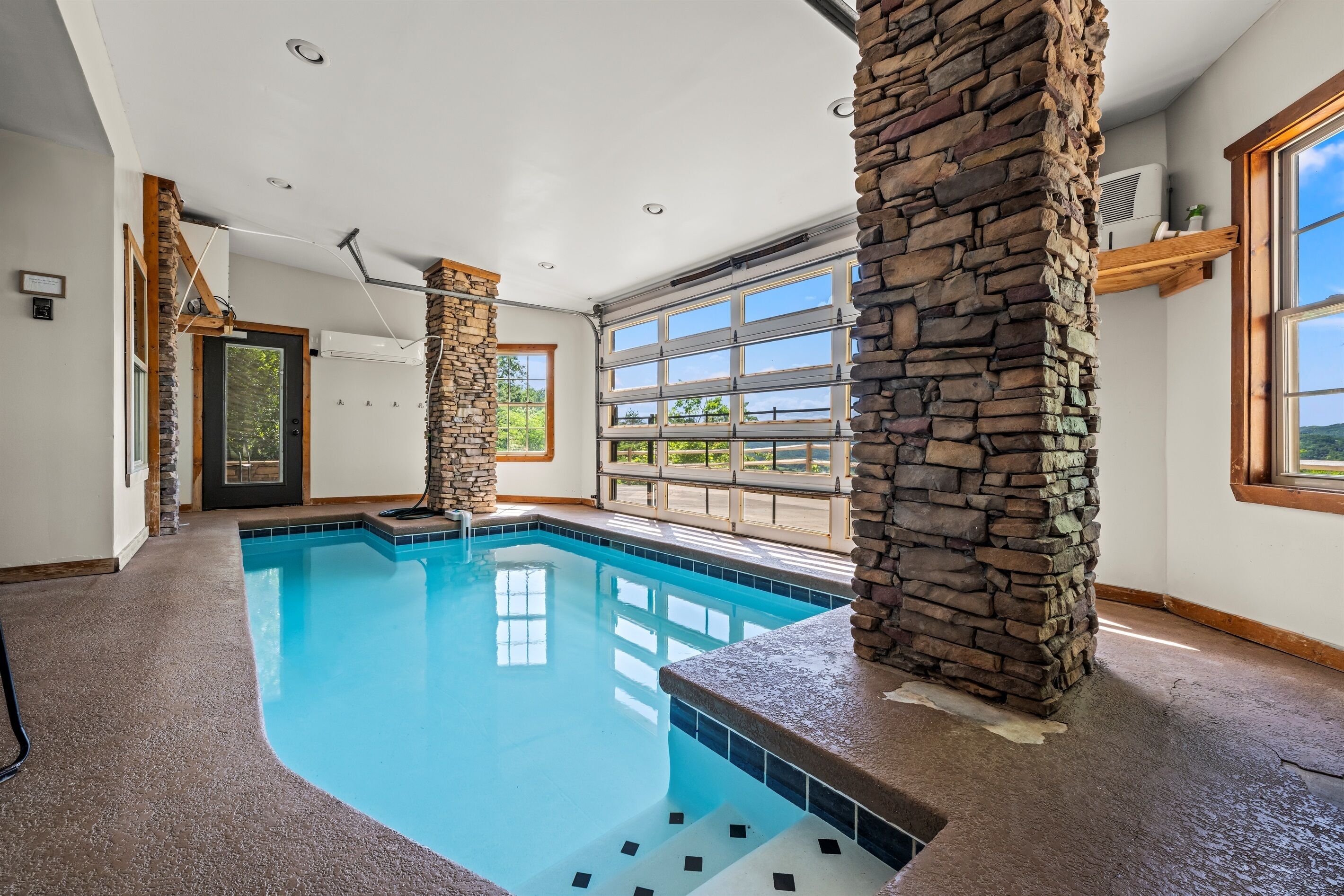 An indoor swimming pool with stone pillars, large windows, and a view of the outdoors.