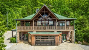A two-story log cabin with a green roof, a balcony, and a garage. - Massive Views+Indoor Pool+Movie Theater+Fire Pit (Sevierville)