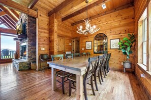 A wooden interior with a stone fireplace, a chandelier, and a dining area with chairs and a table.