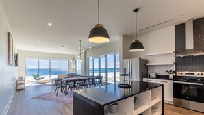 Et moderne køkken med en stor ø, rustfrie hvidevarer og udsigt til havet.