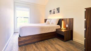 A modern bedroom with a large bed, a wooden nightstand, and a window with blinds.