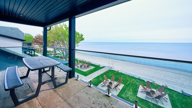 A covered patio with a table and chairs, overlooking a beach and ocean.