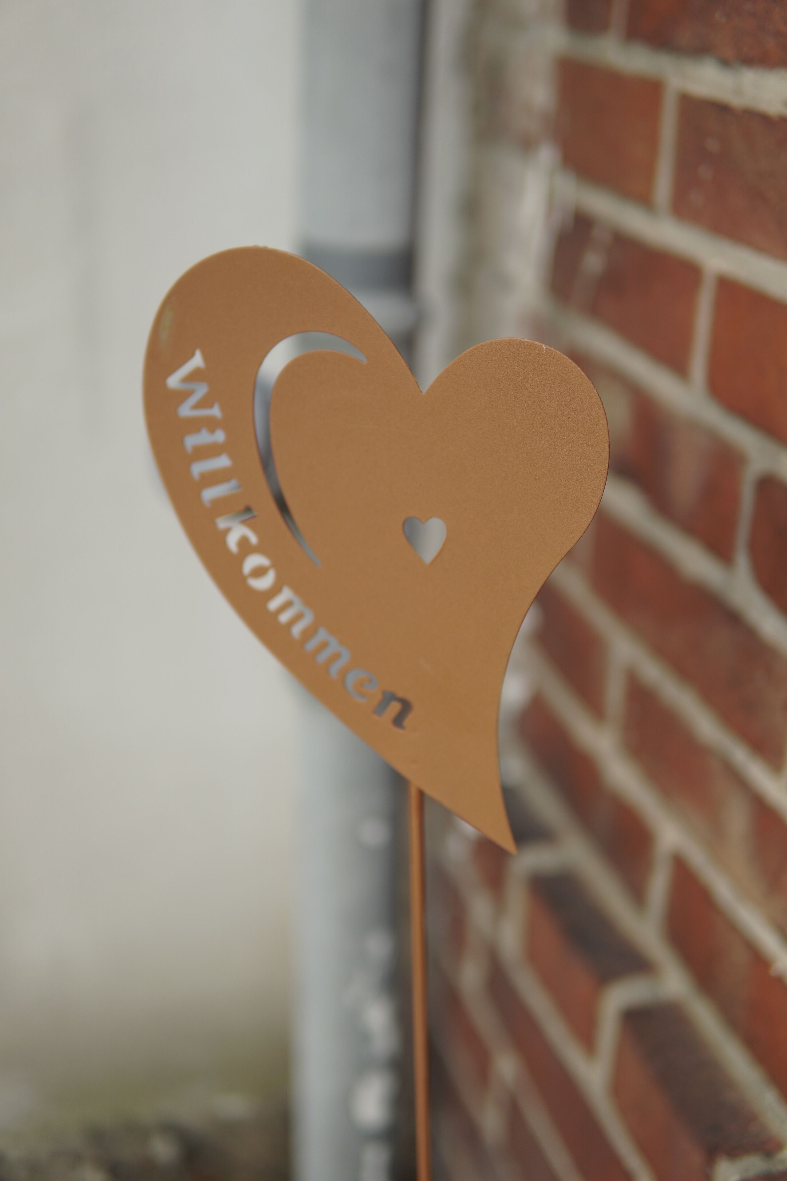 Un letrero con forma de corazón que dice 'Willkommen', sujeto a un palo.