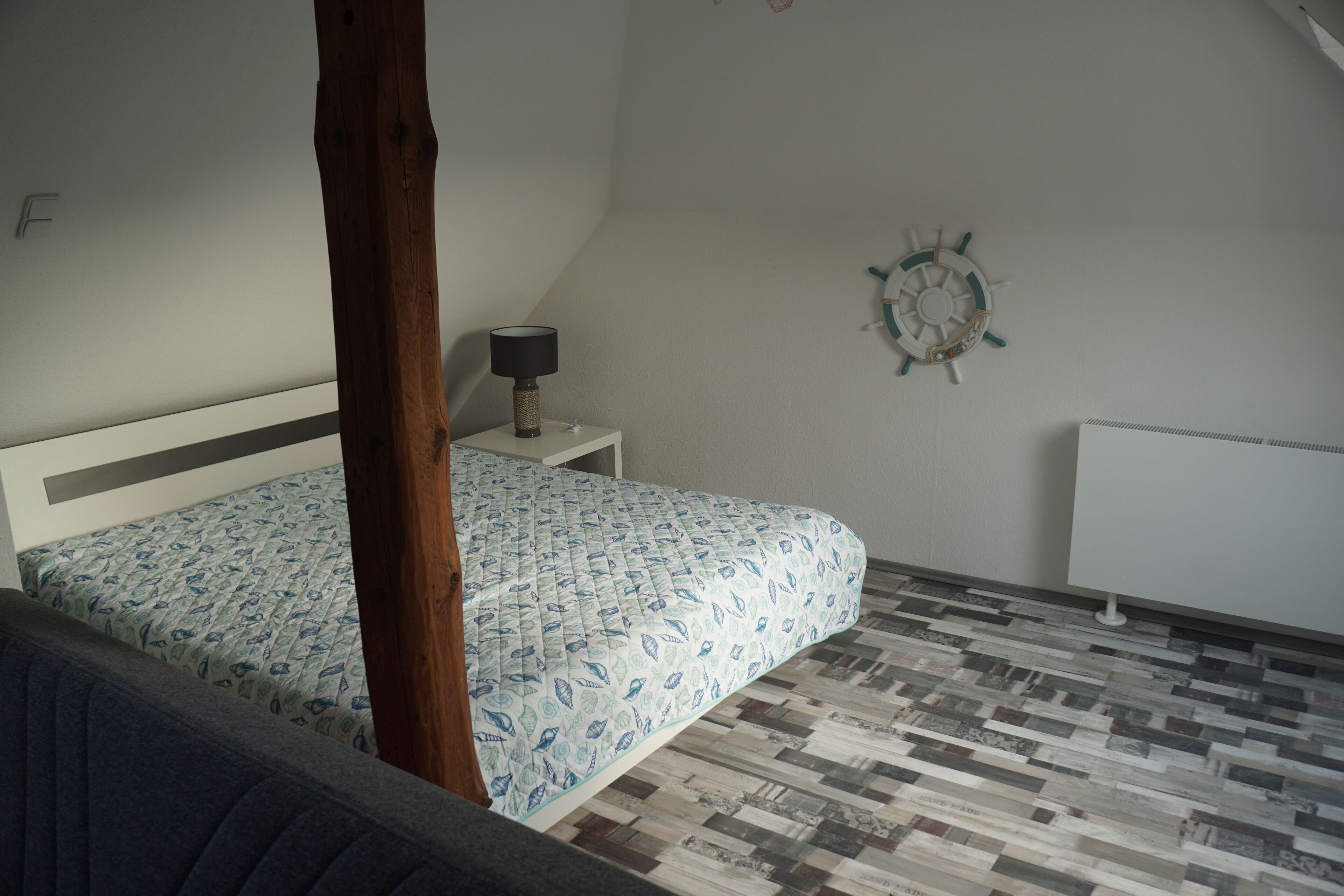 A bedroom with a bed, a nightstand, a wall clock, and a radiator.