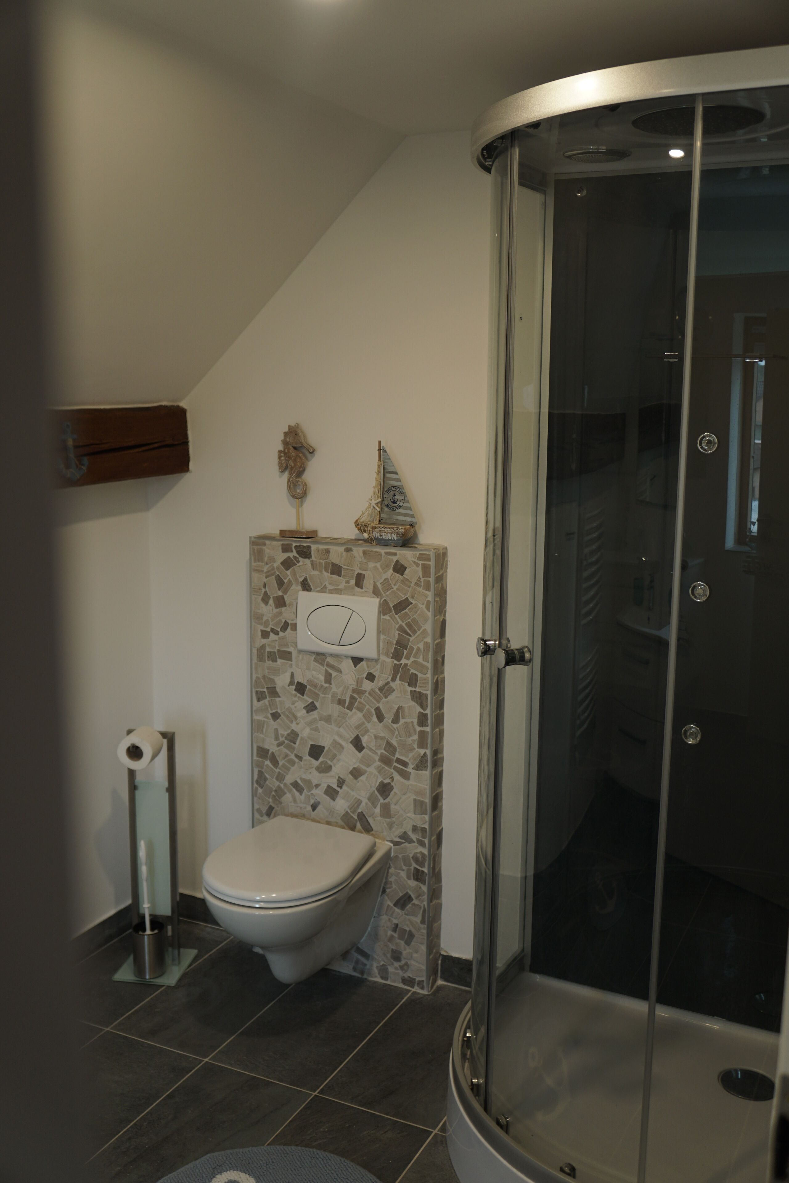 Une salle de bain comprenant des toilettes, un espace douche et un mur décoré de mosaïques.