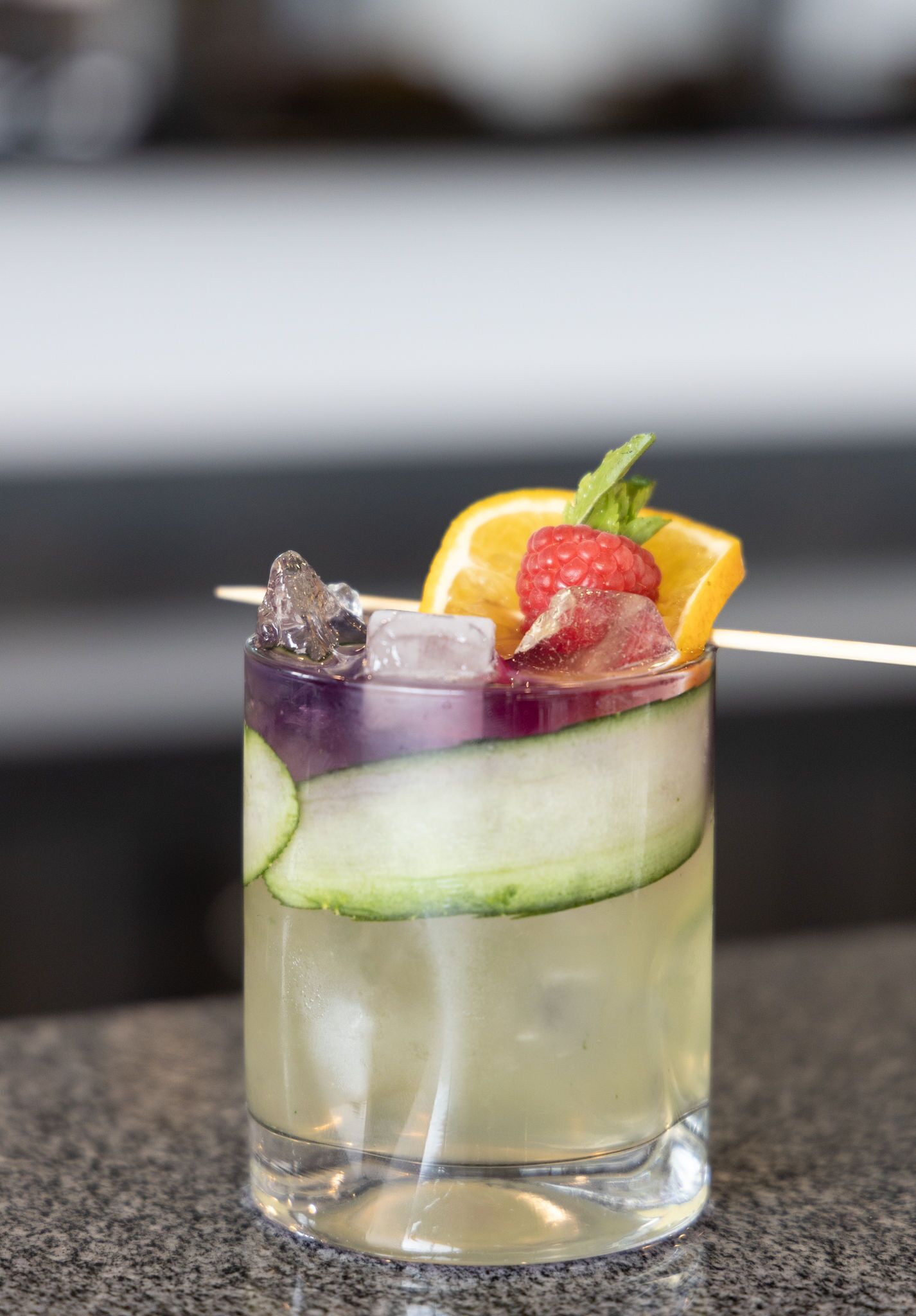 A clear glass with a layered drink, ice cubes, a strawberry, and an orange slice.