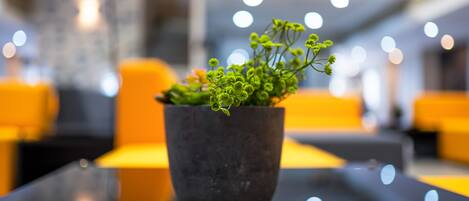 Una planta en maceta sobre una mesa negra reflectante en un interior moderno con asientos amarillos.