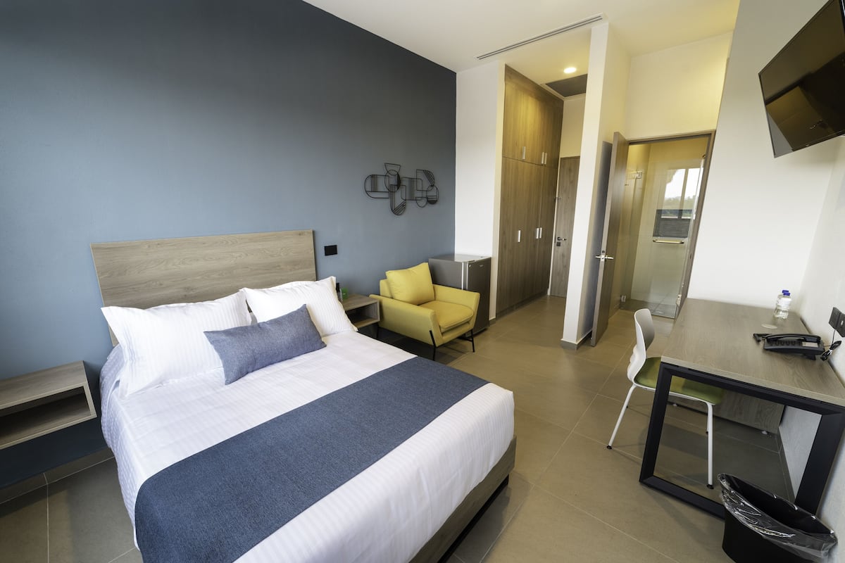 A modern hotel room with a large bed, a desk, a chair, and a wardrobe.