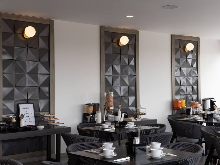 A modern dining area with high tables and chairs, a buffet with various food items, and a welcome sign.