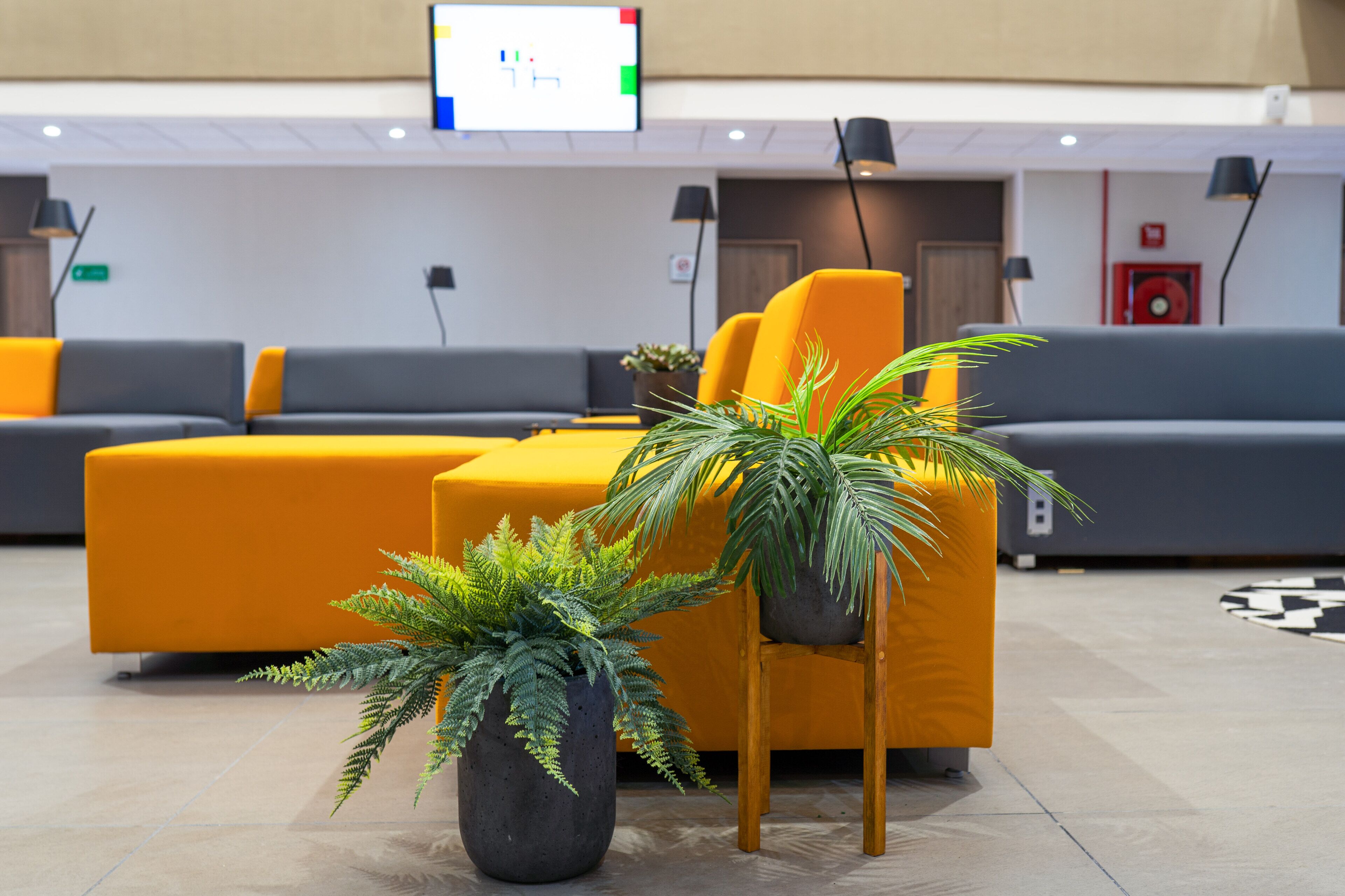 A modern lobby with a sofa set, a potted plant, and a digital screen.