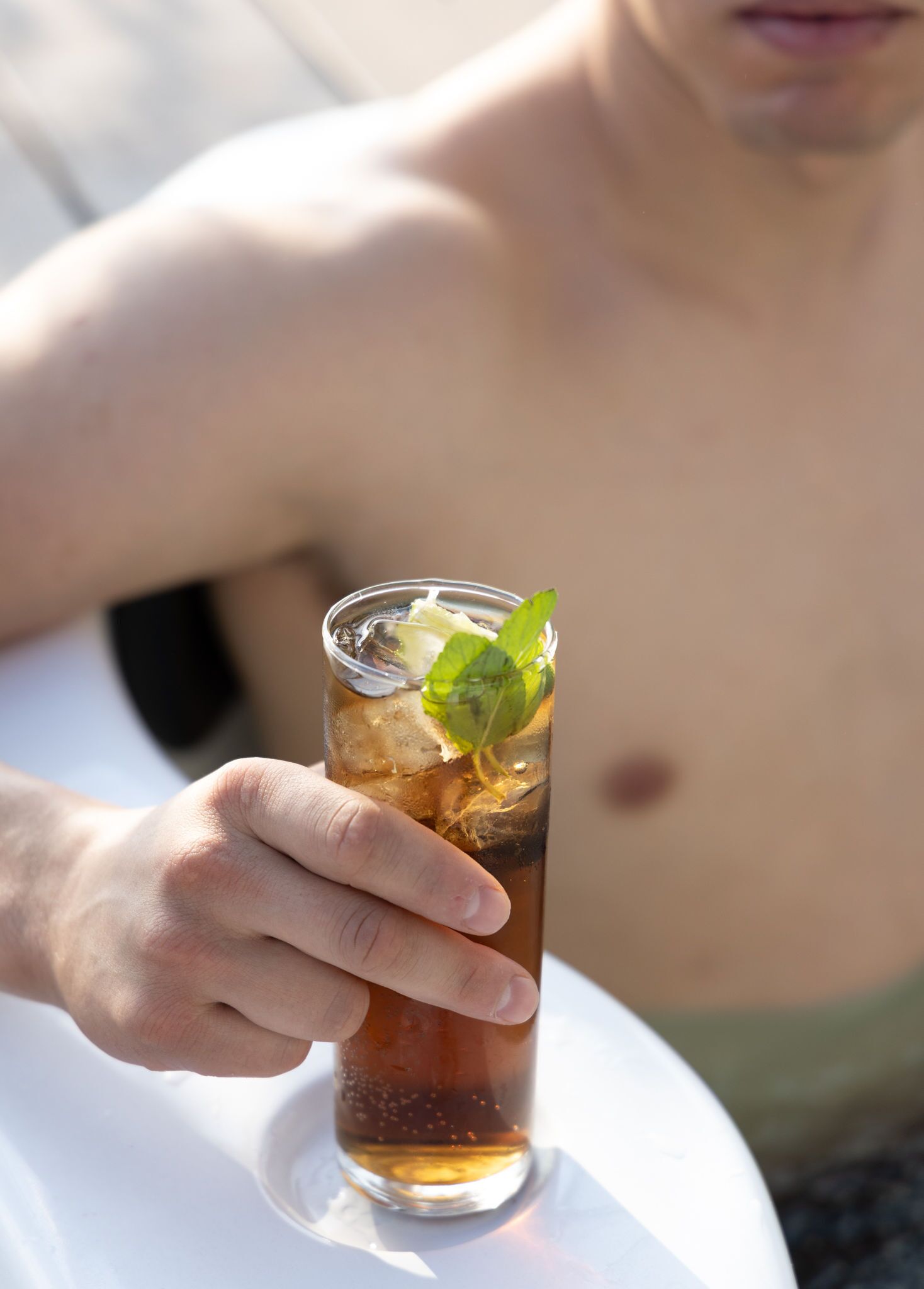 A person holding a glass of iced tea with mint leaves, with a blurred background.