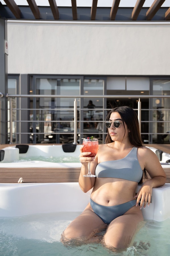 Una persona en una piscina con jacuzzi, usando traje de baño azul y sosteniendo una bebida.