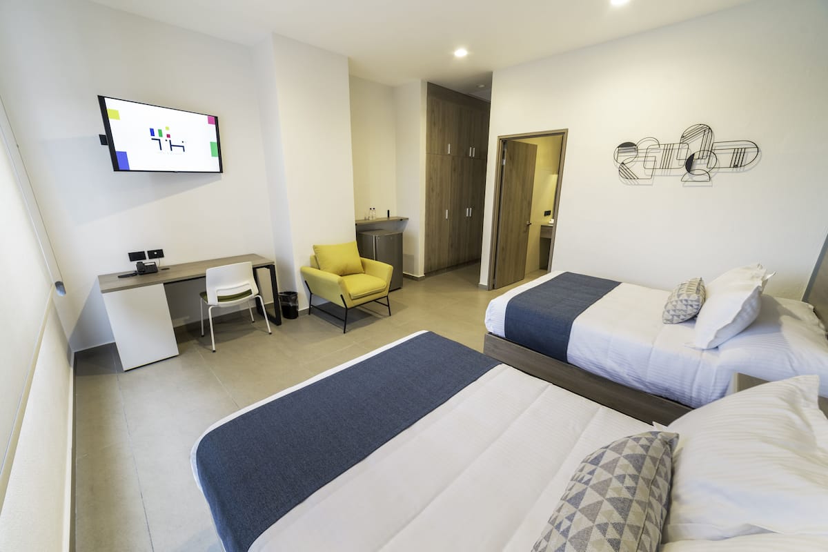 A hotel room with two beds, a desk, a chair, a TV, and a wardrobe.