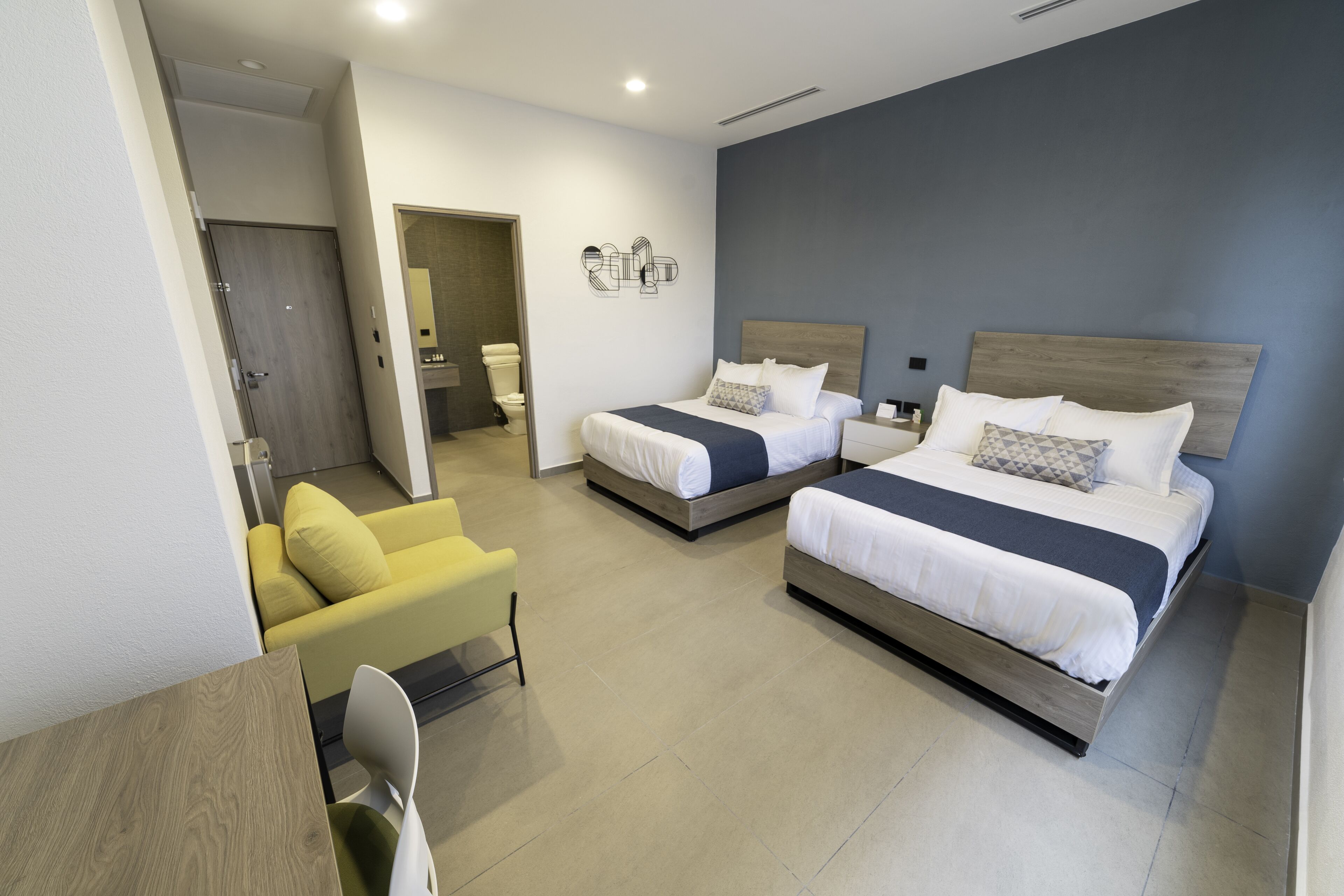 Quarto de hotel com duas camas, uma escrivaninha e uma cadeira.