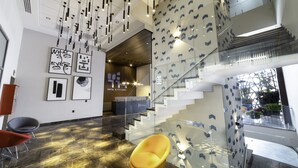 Een moderne hotellobby met een glazen trap, een receptiebalie en eigentijdse kunstwerken.