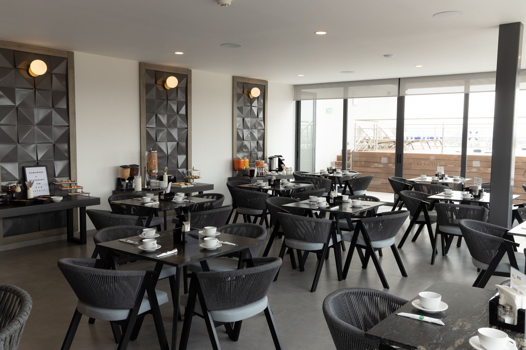 Ein modernes Restaurant mit schwarzen Stühlen und Tischen, einer Bar und großen Fenstern mit Blick auf die Stadt.