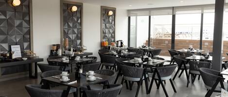 Un restaurant moderne avec des chaises et des tables noires, un bar et de grandes fenêtres donnant sur la ville.