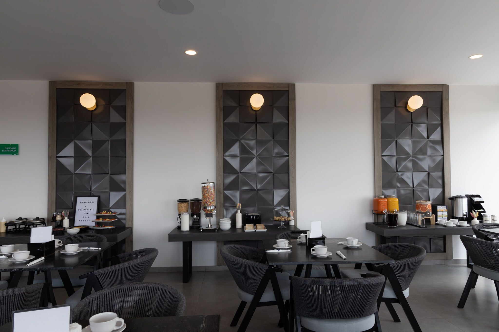 A modern dining area with high tables, wicker chairs, and a buffet setup.