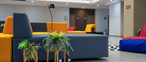 A modern lobby with a large sofa, a small table with plants, and a television screen.