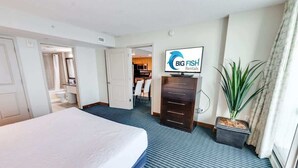 A hotel room with a bed, a TV, a potted plant, and a sign for Big Fish Rentals. - 7th Floor! Modern Building, Direct Oceanfront View (Myrtle Beach)