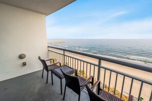 Un balcon doté de meubles en osier, donnant sur une plage et une jetée.