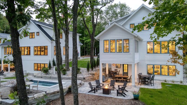A large, two-story house with a covered patio area featuring outdoor furniture and a fire pit. - Traverse City Lakemore Resort, Side by Side Luxury Lakefront Homes on Arbutus Lk (Traverse City)