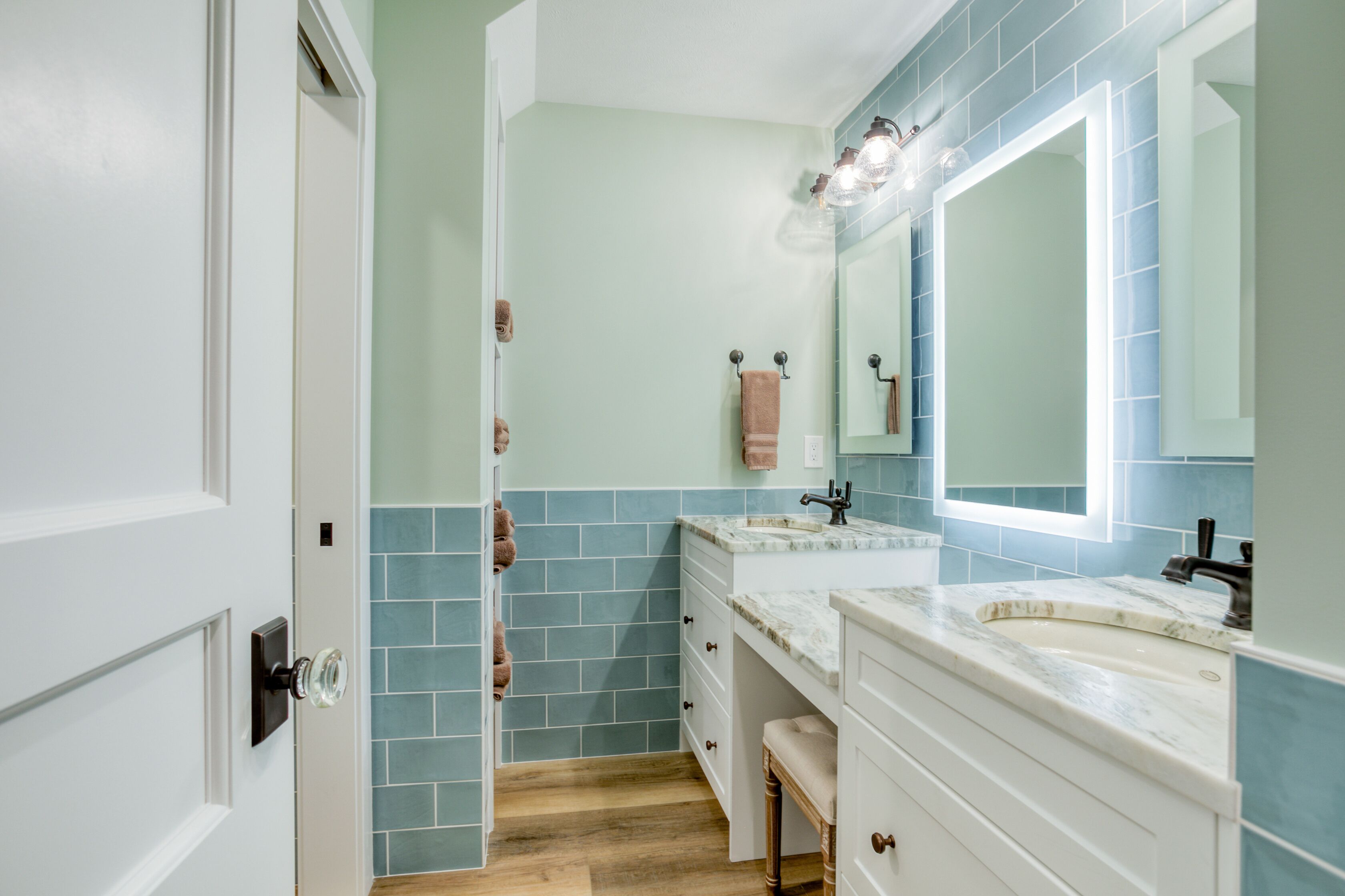 A bathroom with a white vanity, a large mirror, and blue tiles.