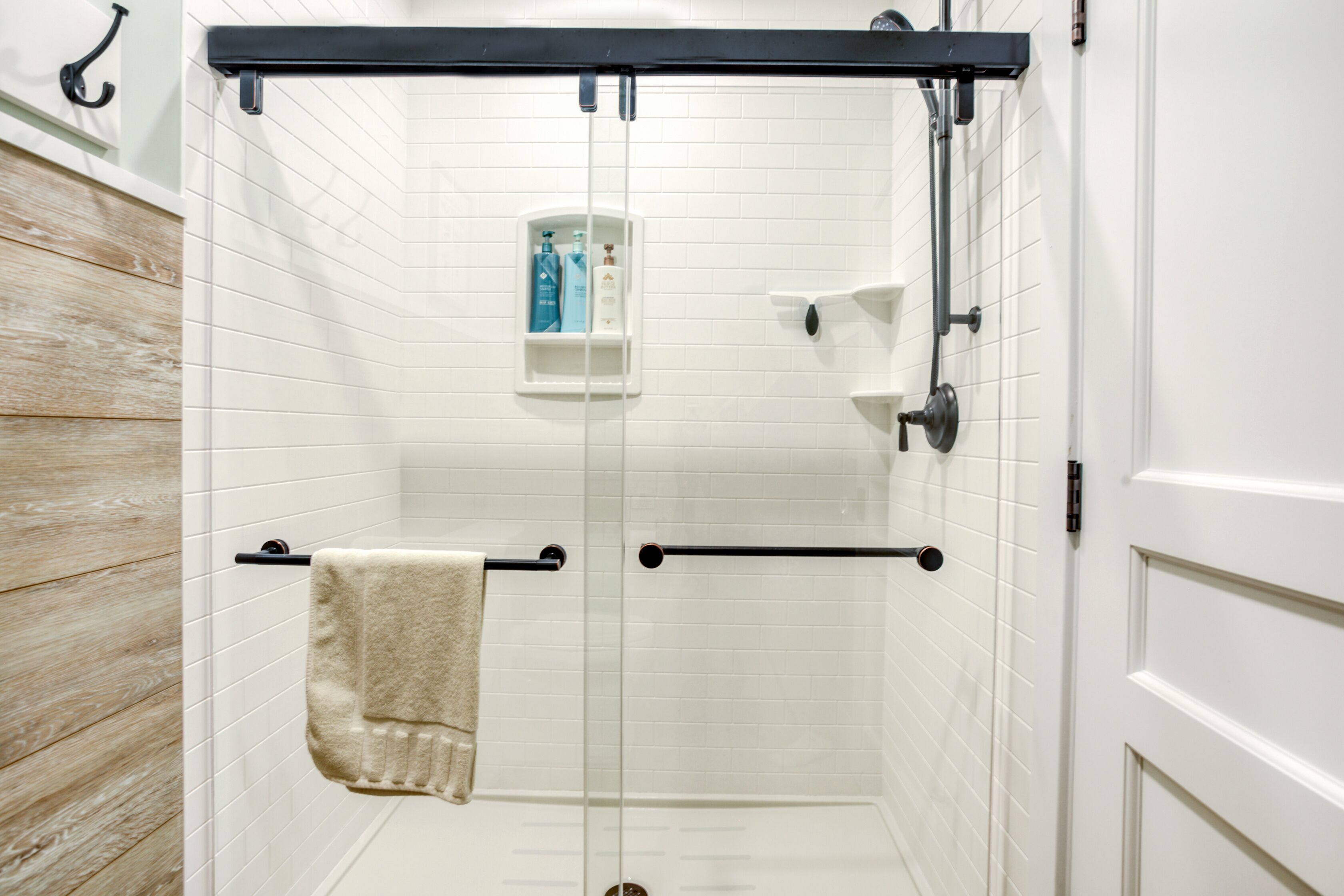 A shower area with a glass door, a towel rack, and a shelf with toiletries.