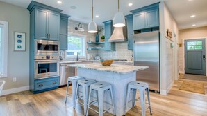A modern kitchen with blue cabinets, a large island with stools, stainless steel appliances, and pendant lighting. - Traverse City Lakemore Resort, Side by Side Luxury Lakefront Homes on Arbutus Lk (Traverse City)