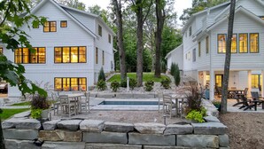 A two-story white house with a stone retaining wall, outdoor seating, and a small pool. - Traverse City Lakemore Resort, Side by Side Luxury Lakefront Homes on Arbutus Lk (Traverse City)