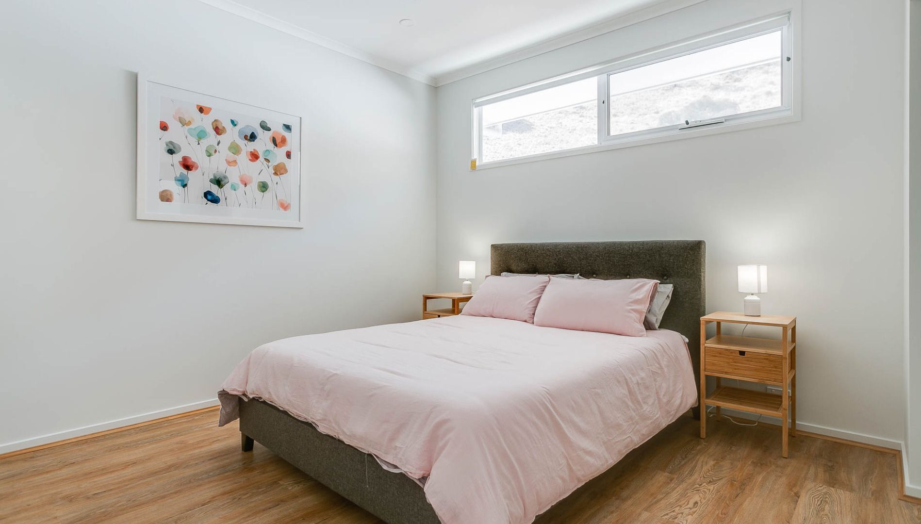 A bedroom with a bed, two bedside tables, a window, and a wall-mounted artwork.