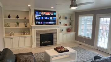 Una sala de estar con chimenea, televisor de pantalla plana montado encima y ventilador de techo.