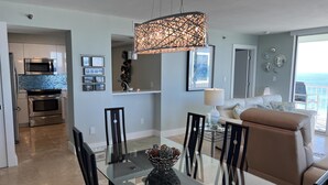 A modern kitchen with stainless steel appliances, a dining area with a glass table, and a living room with a view of the ocean. - Luxurious 15th Floor Penthouse, Water Views -15B (Pensacola Beach)