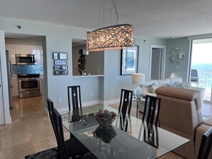 A modern kitchen with stainless steel appliances, a dining area with a glass table, and a living room with a view of the ocean.