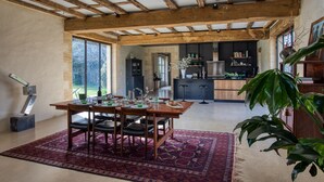 A spacious dining area with a wooden table and chairs, a patterned rug, and a view of the kitchen in the background.