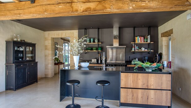 A modern kitchen with a central island, bar stools, wooden cabinets, and a built-in stove.